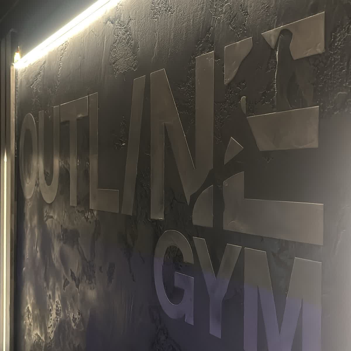 Outline Gym metal logo set into a textured plaster wall